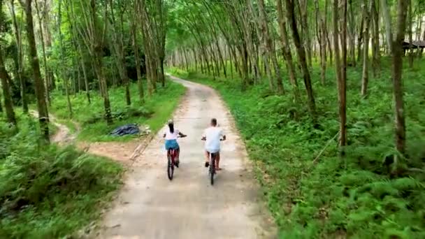 ヤオヤイ島のジャングルの中で自転車に乗っている男性と女性タイのゴム農園に沿って自転車に乗っている男性と女性 — ストック動画