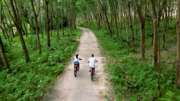 ヤオヤイ島のジャングルの中で自転車に乗っている男性と女性タイのゴム農園に沿って自転車に乗っている男性と女性 — ストック動画