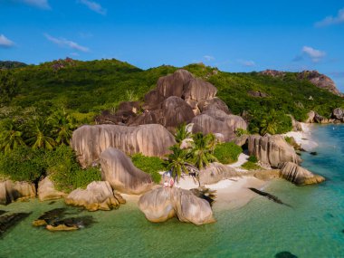 Anse Source dArgent plajı, La Digue Adası, Seyshelles, La Digue Seyşeller 'in insansız hava görüntüsü tropik adanın kuş bakışı görüntüsü, günbatımında sahilde yürüyen iki erkek ve kadın.