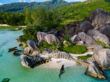 Anse Source dArgent plajı, La Digue Adası, Seyshelles, La Digue Seyşeller 'in insansız hava görüntüsü tropik adanın kuş bakışı görüntüsü, günbatımında sahilde yürüyen iki erkek ve kadın.