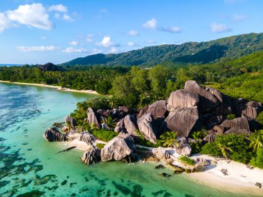 Anse Source dArgent plajı, La Digue Adası, Seyshelles, La Digue Seyşeller 'in insansız hava görüntüsü tropik adanın kuş bakışı görüntüsü, günbatımında sahilde yürüyen iki erkek ve kadın.