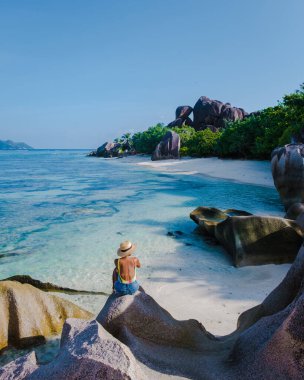 Anse Source dArgent plajı, La Digue Adası, Seyshelles, La Digue Seyşeller 'in insansız hava görüntüsü tropik adanın kuş bakışı görüntüsü, günbatımında sahilde yürüyen iki erkek ve kadın.
