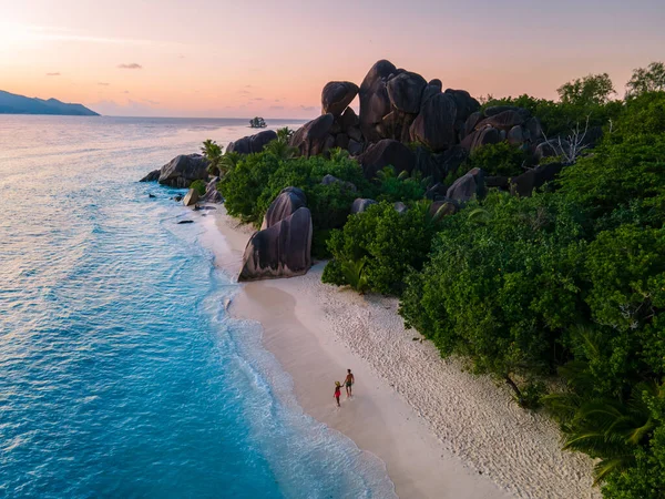 Anse Source dArgent plajı, La Digue Adası, Seyshelles, La Digue Seyşeller 'in insansız hava görüntüsü tropik adanın kuş bakışı görüntüsü, günbatımında sahilde yürüyen iki erkek ve kadın.