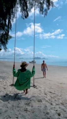 Tayland 'da plajda Naka Adası Phuket Tayland' da salıncakta sallanan bir çift kadın ve erkek. Asyalı kadın ve Avrupalı adam Tayland 'da sahilde