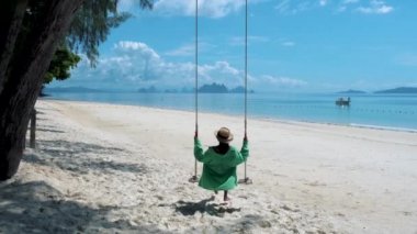 Tayland 'da plajda Naka Adası Phuket Tayland' da salıncakta sallanan bir çift kadın ve erkek. Asyalı kadın ve Avrupalı adam Tayland 'da sahilde