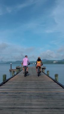 Tayland 'da Phuket yakınlarında bir tropikal adada bisiklete binen iki erkek ve bir kadın, Naka Adası' ndaki bir rıhtımda iki erkek ve bir kadın bisikleti.. 