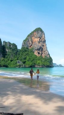 Railay Beach Krabi Tayland, bir çift Asyalı kadın ve Avrupalı erkek Railay Krabi 'nin tropik plajında yürüyorlar.. 