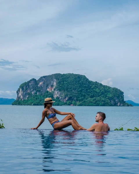 couple European man and an Asian woman in an infinity pool in Thailand looking out over the ocean, a luxury vacation in Thailand.