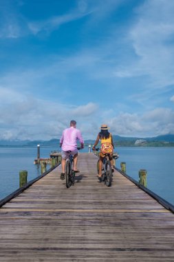 Bisikletli bir adam ve kadın, Tayland 'daki Phuket Naka Adası' ndaki ahşap iskeleli tropikal bir adada bir çift kadın ve erkek.. 