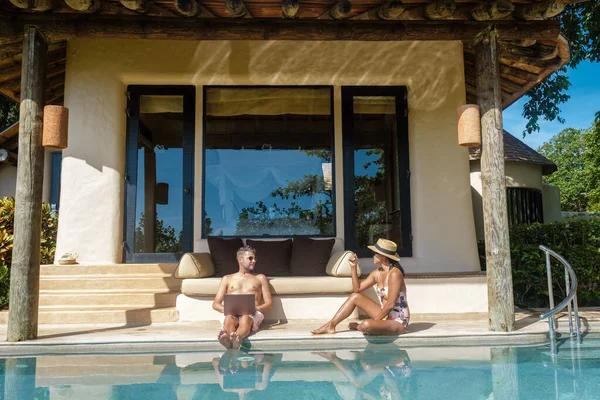 Uzaktan kumandalı çalışan dijital göçebe erkekler ve kadınlar ve dizüstü bilgisayar güneşli bir turkuaz su havuzunda özel bir havuz villasında oturuyor, iş adamı Tayland 'da model dizüstü bilgisayar kullanıyor.. 