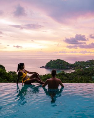 Genç bir çift, tropik bir adada tatil yaparken yüzme havuzunda. Erkek ve kadın gün batımında sonsuz havuzda. Tayland 'da lüks bir havuz villasında lüks bir tatil.