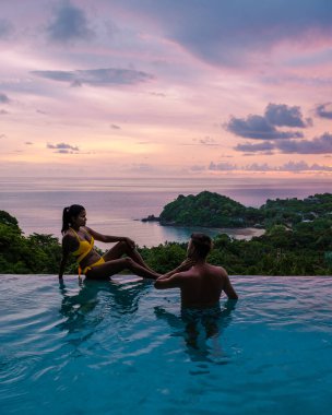 Genç bir çift, tropik bir adada tatil yaparken yüzme havuzunda. Erkek ve kadın gün batımında sonsuz havuzda. Tayland 'da lüks bir havuz villasında lüks bir tatil.