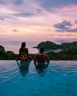 Genç bir çift, tropik bir adada tatil yaparken yüzme havuzunda. Erkek ve kadın gün batımında sonsuz havuzda. Tayland 'da lüks bir havuz villasında lüks bir tatil.