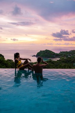 Genç bir çift, tropik bir adada tatil yaparken yüzme havuzunda. Erkek ve kadın gün batımında sonsuz havuzda. Tayland 'da lüks bir havuz villasında lüks bir tatil.