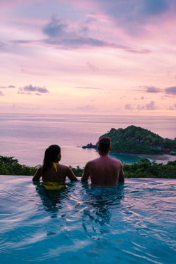 Genç bir çift, tropik bir adada tatil yaparken yüzme havuzunda. Erkek ve kadın gün batımında sonsuz havuzda. Tayland 'da lüks bir havuz villasında lüks bir tatil.