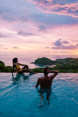 Genç bir çift, tropik bir adada tatil yaparken yüzme havuzunda. Erkek ve kadın gün batımında sonsuz havuzda. Tayland 'da lüks bir havuz villasında lüks bir tatil.