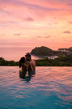 Genç bir çift, tropik bir adada tatil yaparken yüzme havuzunda. Erkek ve kadın gün batımında sonsuz havuzda. Tayland 'da lüks bir havuz villasında lüks bir tatil.