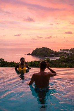 Genç bir çift, tropik bir adada tatil yaparken yüzme havuzunda. Erkek ve kadın gün batımında sonsuz havuzda. Tayland 'da lüks bir havuz villasında lüks bir tatil.