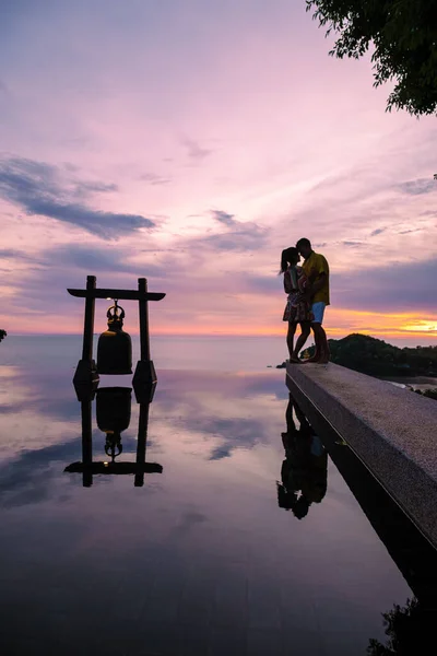 a young couple of men and women at a swimming pool during a vacation on a tropical island. man and woman in infinity pool during sunset. luxury vacation in Thailand pool of a luxury pool villa