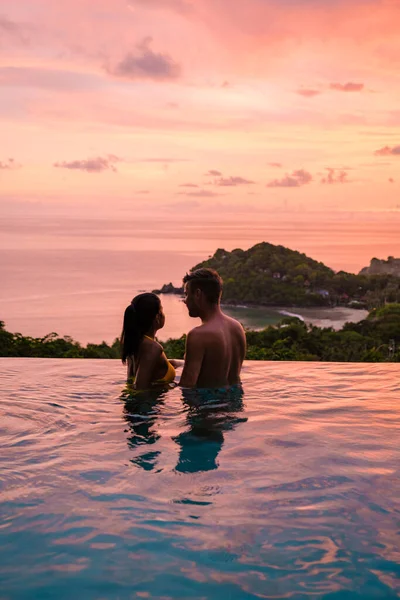 熱帯の島で休暇中にスイミングプールにいた若い男女のカップル 日没時に無限のプールの男と女 豪華なプールヴィラのタイプールでの豪華な休暇 — ストック写真