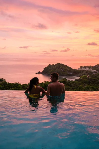 a young couple of men and women at a swimming pool during a vacation on a tropical island. man and woman in infinity pool during sunset. luxury vacation in Thailand pool of a luxury pool villa