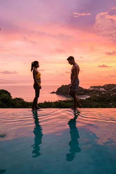 a young couple of men and women at a swimming pool during a vacation on a tropical island. man and woman in infinity pool during sunset. luxury vacation in Thailand pool of a luxury pool villa