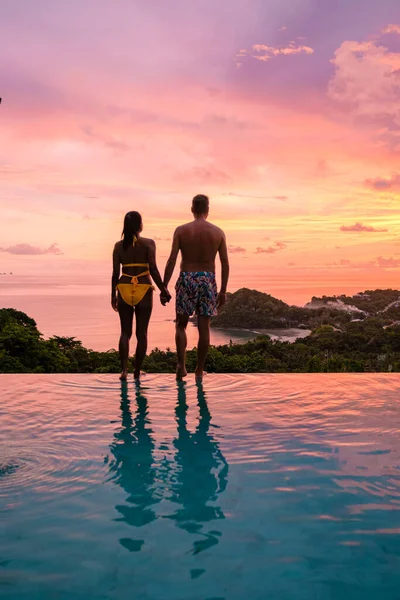 a young couple of men and women at a swimming pool during a vacation on a tropical island. man and woman in infinity pool during sunset. luxury vacation in Thailand pool of a luxury pool villa