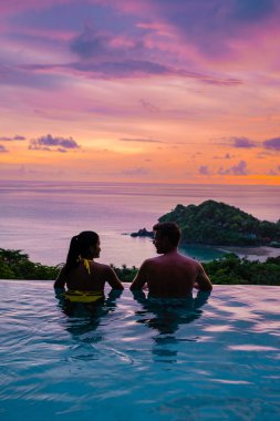 Genç bir çift, tropik bir adada tatil yaparken yüzme havuzunda. Erkek ve kadın gün batımında sonsuz havuzda. Tayland 'da lüks bir havuz villasında lüks bir tatil.