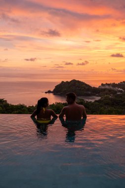 Genç bir çift, tropik bir adada tatil yaparken yüzme havuzunda. Erkek ve kadın gün batımında sonsuz havuzda. Tayland 'da lüks bir havuz villasında lüks bir tatil.