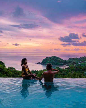 Genç bir çift, tropik bir adada tatil yaparken yüzme havuzunda. Erkek ve kadın gün batımında sonsuz havuzda. Tayland 'da lüks bir havuz villasında lüks bir tatil.