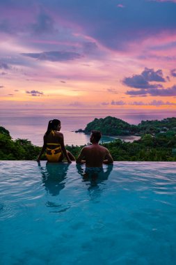 Genç bir çift, tropik bir adada tatil yaparken yüzme havuzunda. Erkek ve kadın gün batımında sonsuz havuzda. Tayland 'da lüks bir havuz villasında lüks bir tatil.