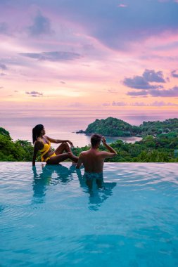 Tayland 'da sonsuz havuzda, okyanusa bakan bir çift Avrupalı erkek ve Asyalı bir kadın Tayland' da lüks bir tatil. Phuket
