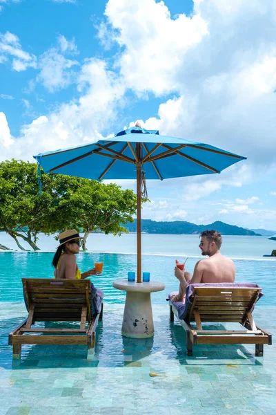 couple European man and an Asian woman in an infinity pool in Thailand looking out over the ocean, a luxury vacation in Thailand. Phuket, pool with beach chairs and umbrella with blue ocean