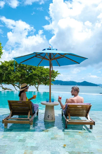 couple European man and an Asian woman in an infinity pool in Thailand looking out over the ocean, a luxury vacation in Thailand. Phuket, pool with beach chairs and umbrella with blue ocean