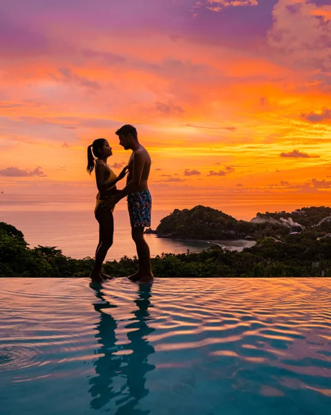 タイのインフィニティプールでヨーロッパ人男性とアジア人女性のカップルが海を眺め タイの豪華な休暇を過ごします プーケット — ストック写真