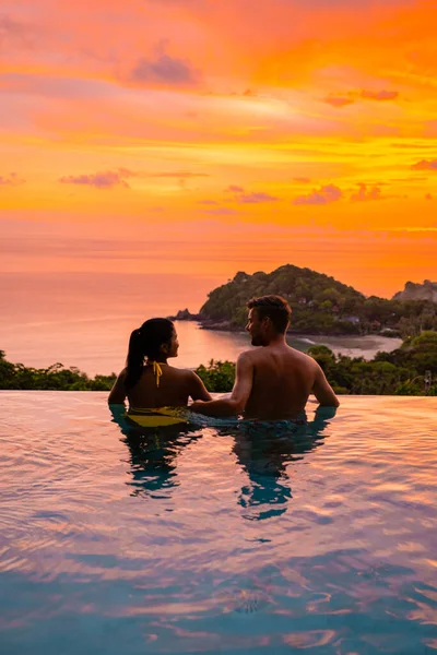 couple European man and an Asian woman in an infinity pool in Thailand looking out over the ocean, a luxury vacation in Thailand. Phuket