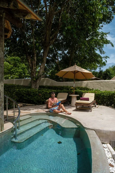 European man at infinity pool looking out over the ocean, luxury vacation private pool villa, luxury retreat