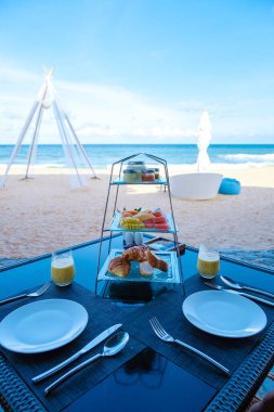 Phuket Tayland 'da kumsalda kahvaltı yemek ve tropikal deniz manzaralı lüks bir kahvaltı masası lüks seyahat ve yaşam tarzı.. 