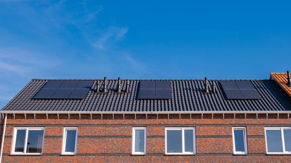 Newly build houses with solar panels attached on the roof against a sunny sky Close up of new building with black solar panels. Zonnepanelen, Zonne energie, Translation: Solar panel, , Sun Energy.