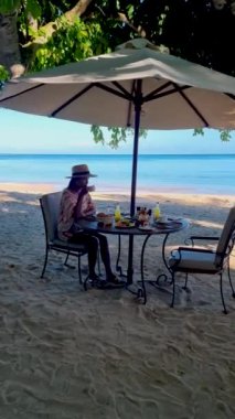 Breakfast on the beach in Thailand, a Luxury breakfast table with food and beautiful tropical sea view background. Asian woman having breakfast