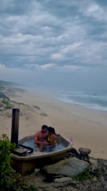 couple in bathtub on the beach of The Hoop nature reserve in South Africa, romantic bath tub with rose petals, luxury vacation in a jacuzzi, couple men and woman in bath tub of a luxury resort 