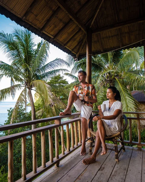 a couple of men and women on the balcony of a beach hut with coffee in Railay beach Krabi Thailand in the morning, men and woman waking up in a backpacker hut in Thailand