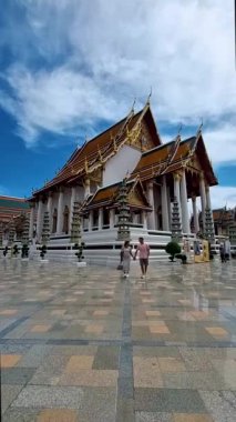 Wat Suthat Thepwararam Ratchaworahawihan Tayland 'ın başkenti Bangkok' taki kraliyet tapınağıdır. İki Avrupalı erkek ve şapkalı Asyalı kadın Bangkok 'ta bir tapınağı ziyaret ediyorlar.