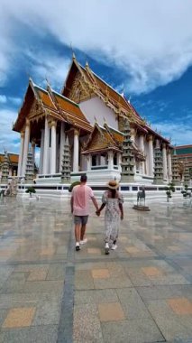 Wat Suthat Thepwararam Ratchaworahawihan Tayland 'ın başkenti Bangkok' taki kraliyet tapınağıdır. İki Avrupalı erkek ve şapkalı Asyalı kadın Bangkok 'ta bir tapınağı ziyaret ediyorlar.