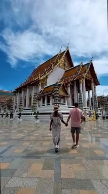 Wat Suthat Thepwararam Ratchaworahawihan is the royal temple in the capital city of Bangkok, Thailand. Couple of European men and Asian woman with hat visit a temple in Bangkok