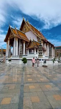 Wat Suthat Thepwararam Ratchaworahawihan is the royal temple in the capital city of Bangkok, Thailand. Couple of European men and Asian woman with hat visit a temple in Bangkok