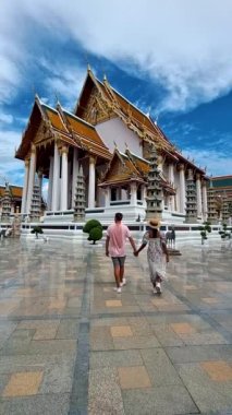 Wat Suthat Thepwararam Ratchaworahawihan is the royal temple in the capital city of Bangkok, Thailand. Couple of European men and Asian woman with hat visit a temple in Bangkok