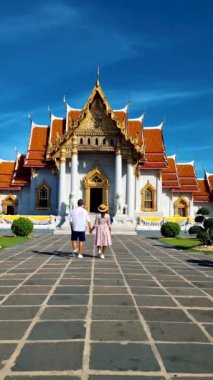 Wat Benchamabophit mermer tapınak, Tayland 'ın başkenti Bangkok' ta bulunan bir kraliyet tapınağıdır. Şapkalı birkaç Asyalı kadın ve Bangkok 'taki bir tapınağı ziyaret eden Avrupalı erkekler.