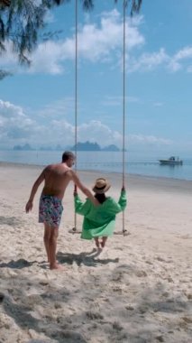 Phuket Thailand Naka Island, a couple of men, and women at a swing on the beach. Tropical beach with a swing. Asian women and European men on the beach with swim short