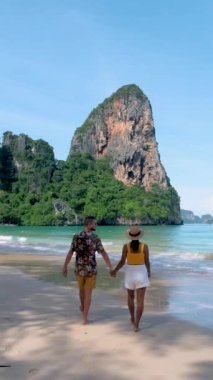 Railay Beach Krabi Tayland, Asyalı kadınlar ve Avrupalı erkekler, sabahları sahilde yürüyen bir çiftin ağır çekimde Tayland Krabi 'de yürümesi.